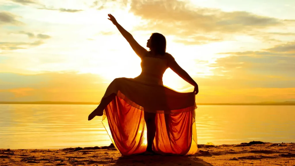 Woman dancing freely on the beach at sunset, symbolizing emotional release and inner freedom.